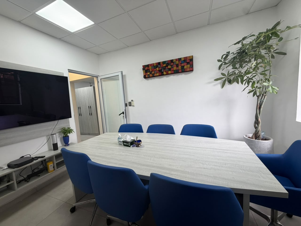 Suite 1A meeting room with conference table, display screen and blue chairs